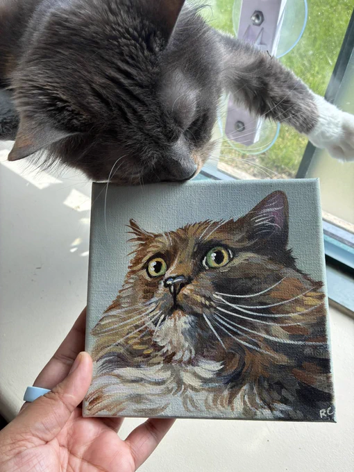 peppercorn the dilute calico lounges in her window seat. beside her, her parent holds up a hand-painted portrait of her that was sent by Chewy. she sniffs the canvas. meeko says, “wow!! Chewy sent my parents this portrait of my sister. it was such a nice surprise.”