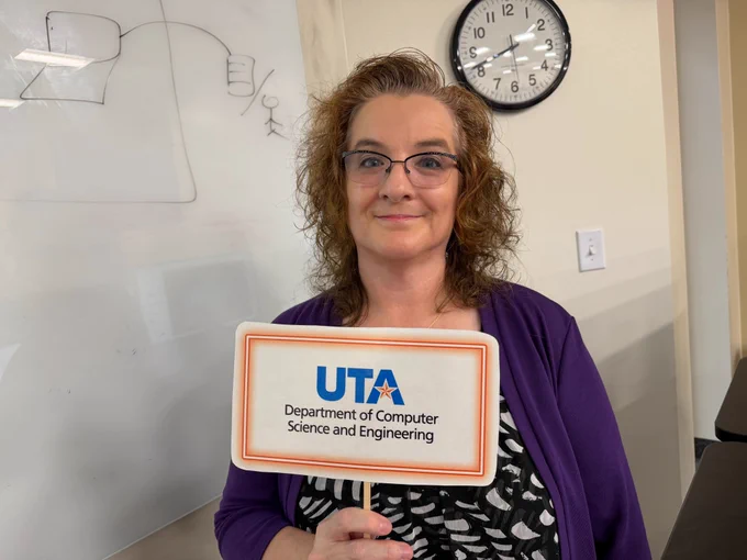 a woman smiles while holding a sign with the UTA CSE logo on it