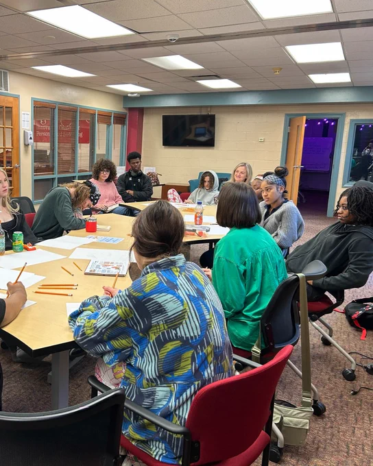 A group of people sitting around a table in a classroom-like setting, engaged in an activity or discussion. 