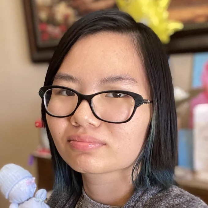 Iris Wang, wearing black glasses and shoulder-length hair, looks at the camera with a slight smile.
