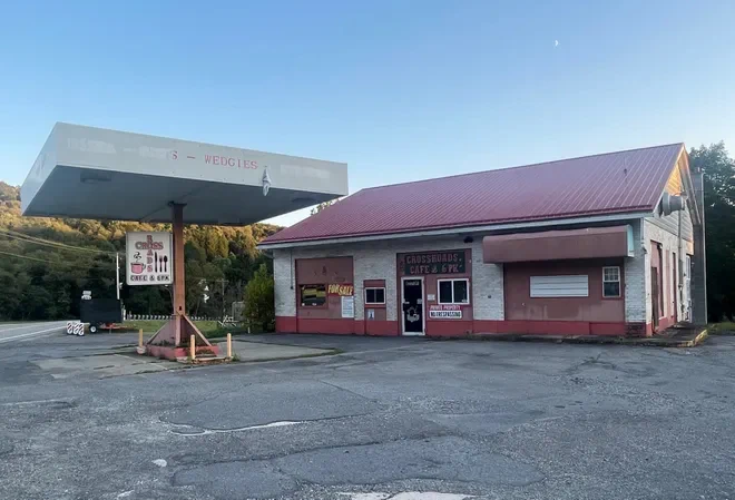 Old gas station with a faded red roof and a canopy over empty fuel pumps in a rural setting at dusk.
