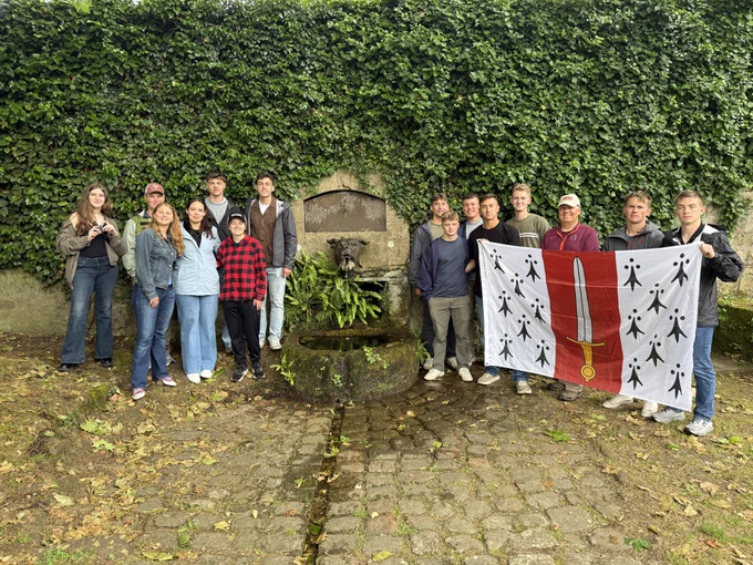 A group of cadets and faculty stand near Devil Dog Fountain, which is shaped like a dog’s head, in the nearby town of Belleau, while some of the cadets hold the Corps of Cadets flag.