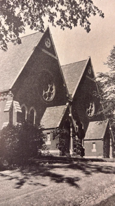 Cornell's Sage Chapel, a historic building with Gothic architectural features, including tall, pointed roofs and large circular windows, as seen in 1926. The structure is surrounded by trees and a pathway runs alongside it. The overall scene has a serene and timeless quality.