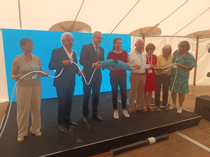 Le préfet des Hautes-Pyrénées aux côtés d’élus, inaugurant le poste électrique d’Aure en branchant une prise électrique bleue à taille humaine fictive. 