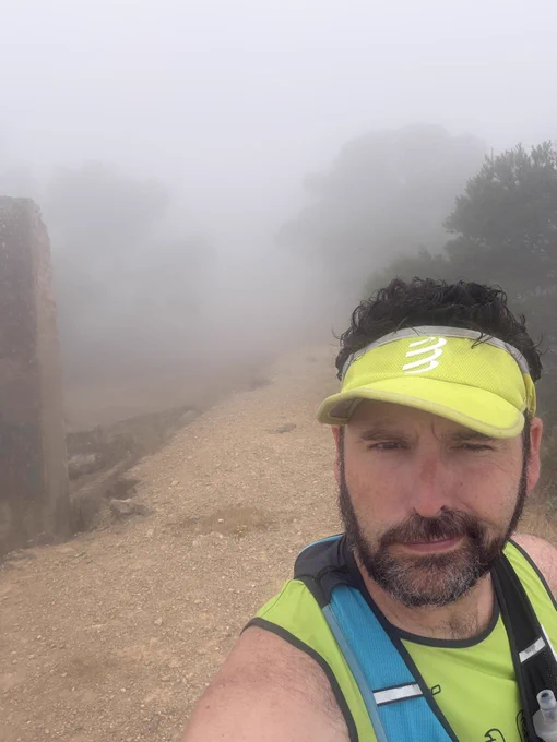 Yo con cara de gilipollas y media sonrisa, con gorra de running y camiseta de tirantes con un paisaje de niebla y árboles al fondo