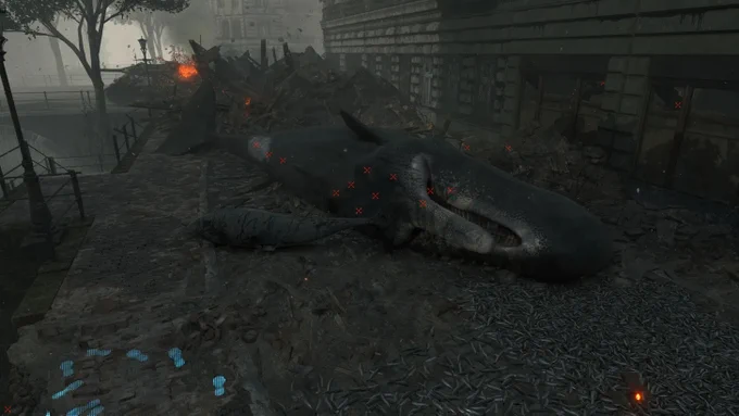 Death Stranding Director's Cut: Riesiger gestrandeter Wal auf Kopfsteinpflaster zwischen Ruinen und Feuer. Roter X-Marker als Spielmechanik über dem Körper. Apokalyptische Stadtszene. Screenshot.