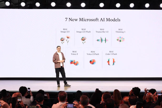 Presenter on stage at Microsoft Build with a large screen showing seven new Microsoft AI models across image, voice, transcription, coding, and reasoning.