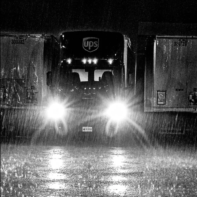 A UPS tractor with bright headlights parked between trailers in heavy rain at night.