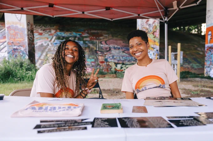 Two people sit at a table under a tent along the Beltline, smiling.