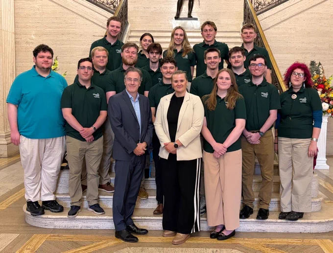 Image of 18 people standing on the steps in the Great Hall at Parliament Buildings – Junior Minister Aisling Reilly with Dr Tim Campbell from the Saint Patrick Centre and young people who are taking part in the Young Ambassador Programme.