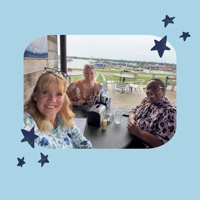 Light blue background with decorative navy stars. There is one photo in the middle of the slide, showing all three women smiling and sitting outside, enjoying a meal together. 