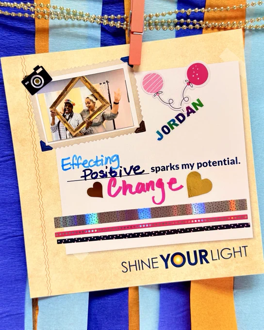 A decorative card displays a photo of two people posing with fun props. Colorful streamers and a string of beads hang above. The card includes uplifting text saying, "Effecting Positive Change sparks my potential," with words "Positive Change" highlighted in colors. The bottom of the card reads, "Shine Your Light," adorned with gold hearts and decorative tape.