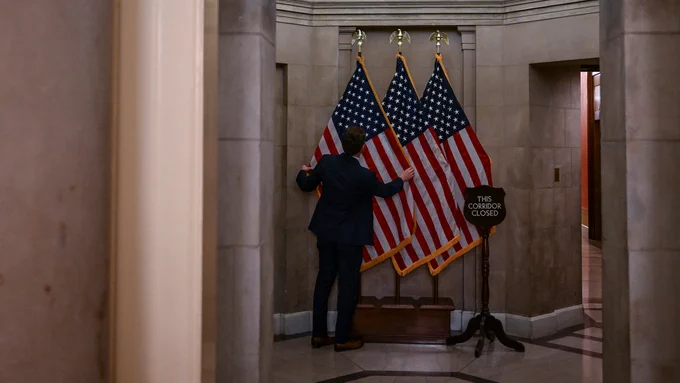 A government employee adjusts an American flag in the U.S. capitol building.