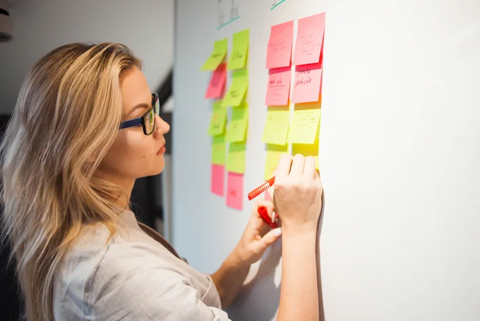 Person writing on colorful sticky notes arranged on a whiteboard during a brainstorming session.