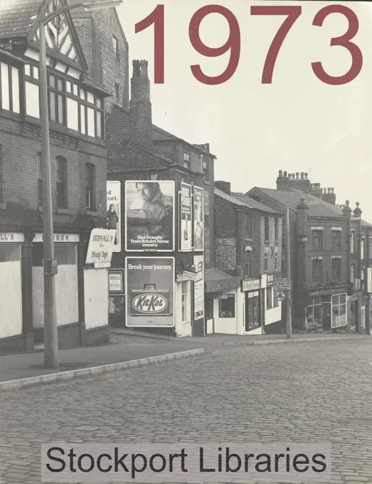 Street scene in 1973 with buildings, cobblestones, and advertisements, including KitKat.