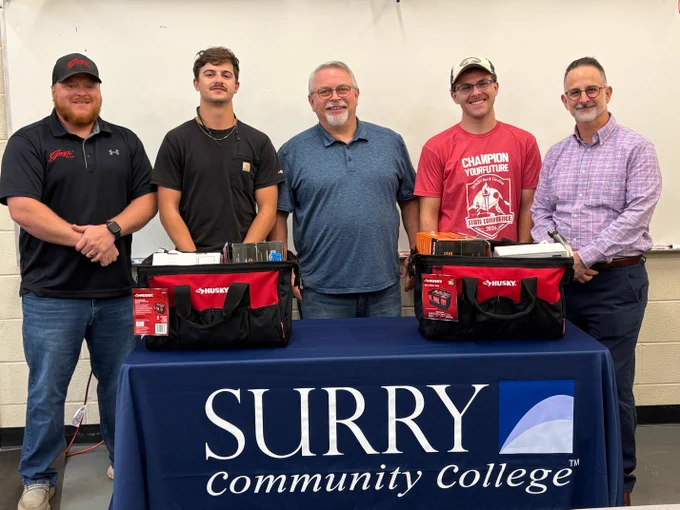 image of five people standing behind a table with tool kits on it