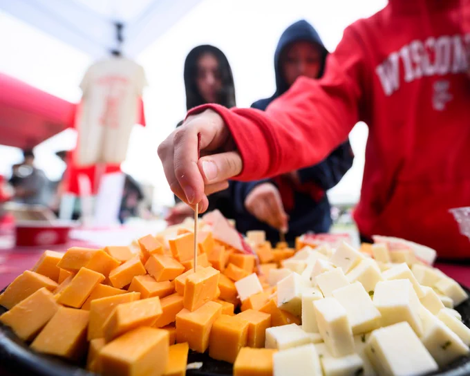 A person grabs a cube of cheese with a toothpick from a platter that has a variety of cheese cubes. 