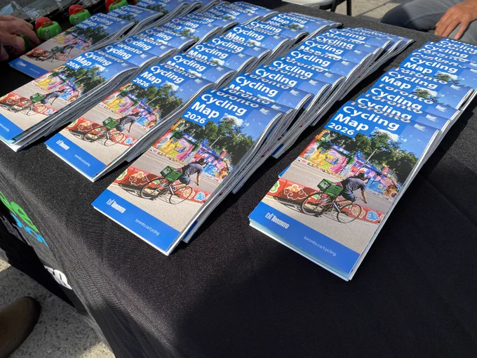 Stacks of 2026 cycling maps laid out on a black tablecloth at Nathan Phillips Square.