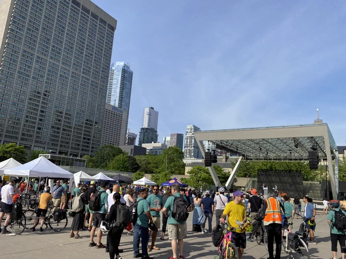 Crowd gathered at Nathan Phillips Square with white tents and a large stage under a clear blue sky in a city park.