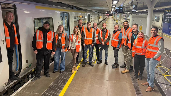 A group of people wearing orange safety vests are standing on a platform at Blackfriars station beside a Thameslink train. 
