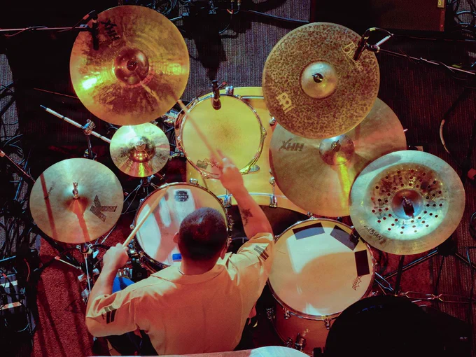 A Marine drummer performs during a live concert, viewed from above, surrounded by a full drum kit and illuminated stage lighting.