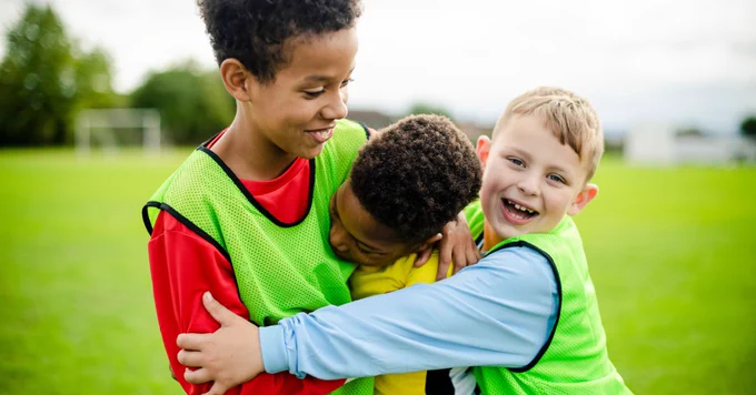 Children wearing green jerseys are joyfully hugging on a soccer field.