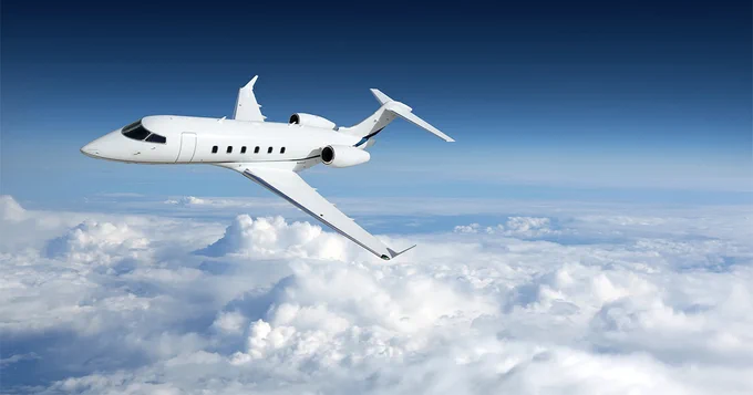 A sleek business jet soars above a layer of fluffy white clouds under a clear blue sky.