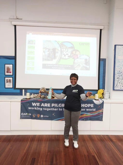 A school volunteer smiling with arms out wide in front of a projection screen. 