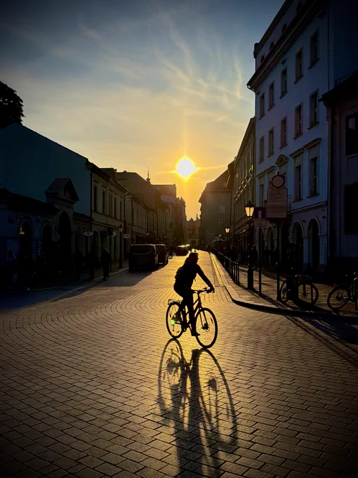 A photo of sunset in Krakow showing a street scene with a silhouette of a cyclist.