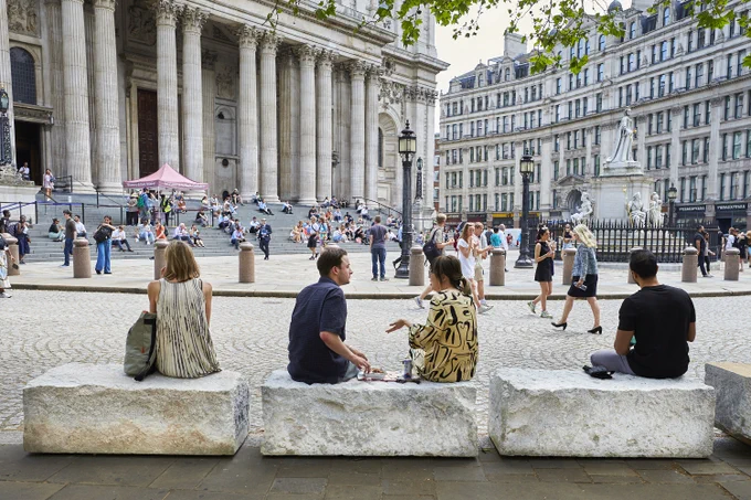 People sit and gather outside St. Paul’s Cathedral in London, with its grand columns, steps, and a nearby monument.