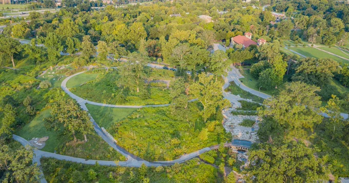An aerial over the Nature Playscape in Forest Park shows the World’s Fair Pavilion on top of Government Hill above a spring winding through a landscape of full-leaf trees and other foliage.