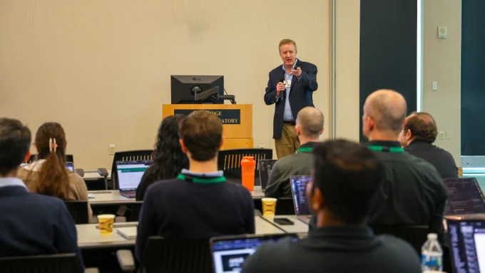 Eric Nielsen speaking to attendees during the Oak Ridge Leadership Computing Facility Annual User Summit at Oak Ridge National Laboratory. Audience members listen while using laptops and taking notes.