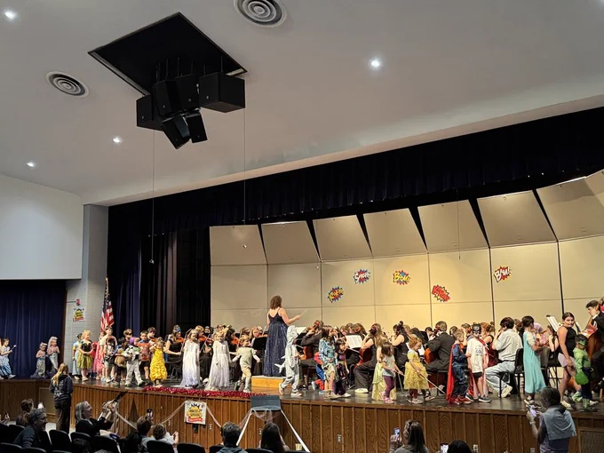 Orchestra Superhero event from May 2026, with students and younger guests on stage.