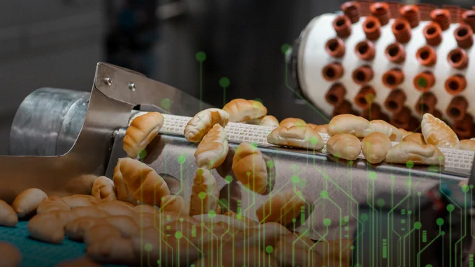 Freshly baked croissants moving along a conveyor belt in an industrial bakery setting.