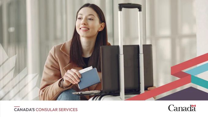 A woman crouches on the ground with her laptop open on top of her carry-on bag. She is holding her passport in her hand. 
Logos: Travel.gc.ca and Canada wordmark
