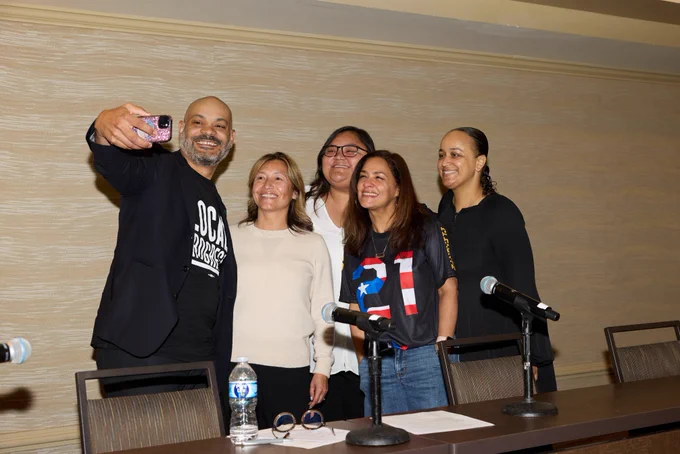 Members and partners taking a selfie in front of a long table with microphones.