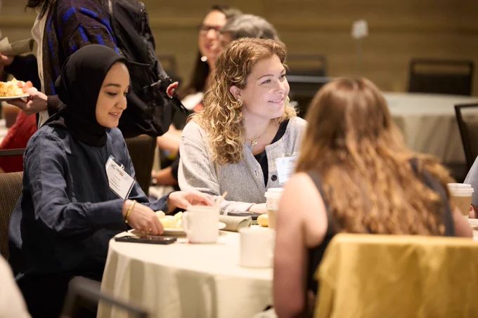 Participants sitting at a table in a conference room listening and smiling.