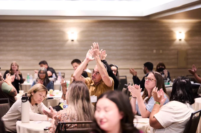 Participants clapping enthusiastically in a conference room. 
