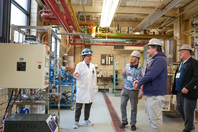 Student in a hardhat talking to alumni in hardhats in a lab.