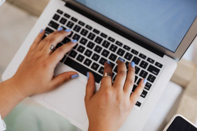 Person with purple nail polish typing on a laptop.