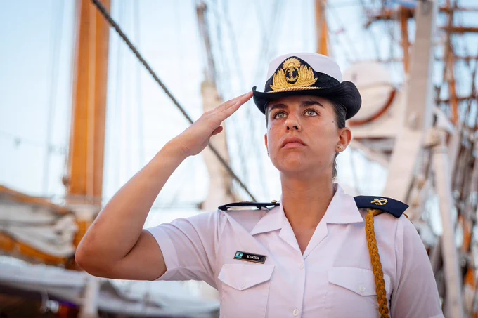 An Argentine sailor stands at attention and renders a salute aboard a tall ship during a ceremonial observance.