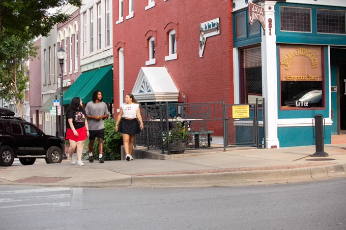 Three friends walking and talking on a sidewalk in downtown Warrensburg, passing by historic brick buildings and the Java Junction coffee shop.