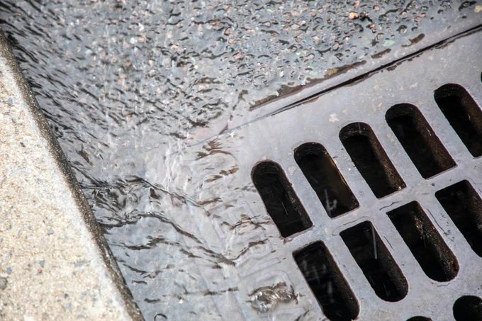 Water flowing into a catch basin on a wet street surface after rainfall.