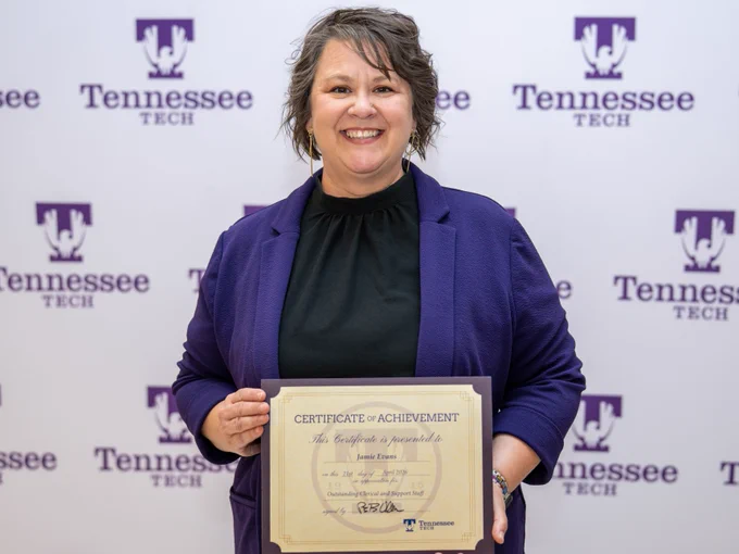 A person holding a certificate of achievement while posing in front of a Tennessee Tech backdrop.