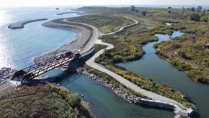 A bridge, connected to various paths, runs along the edge of a lake and beside wetlands.
