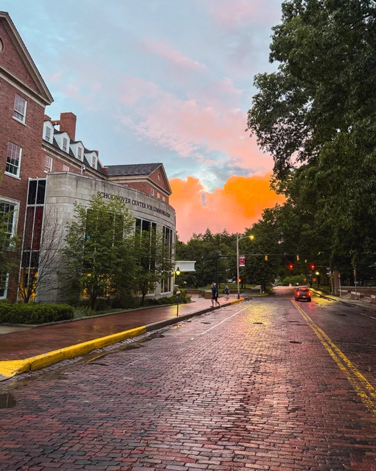Schoonover Center on the left, with the sunset turning clouds orange straight ahead. The brick roadway is wet from rain. 