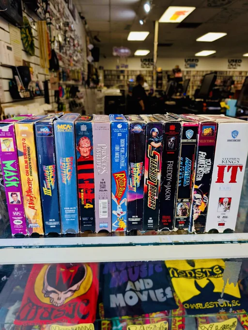 A nostalgic display of VHS tapes in a retro store setting. The mood is vintage with a focus on classic movies.