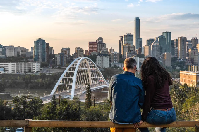Two people sitting on a ledge, enjoying the view of downtown Edmonton and the Walterdale Bridge. 