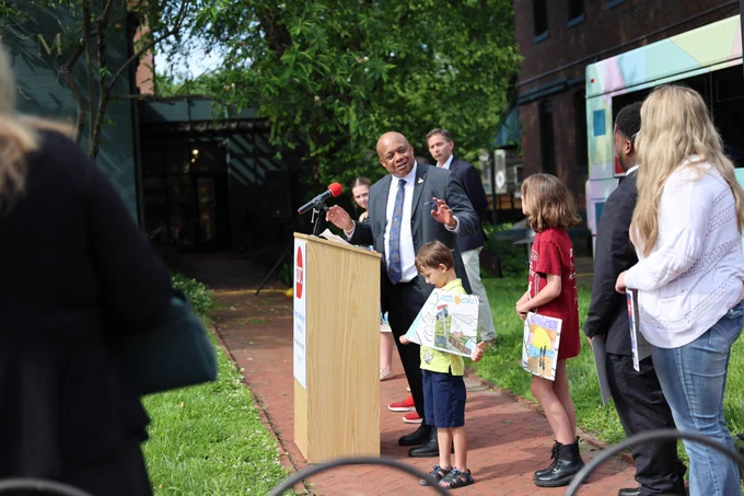 Superintendent Dr. Brian Yearwood speaks at a podium while students and adults stand nearby.