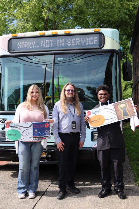 Two students stand with an adult in front of a TARC bus.